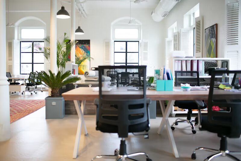 Ufficio luminoso e spazioso con grandi finestre, sedia da lavoro e scrivanie.